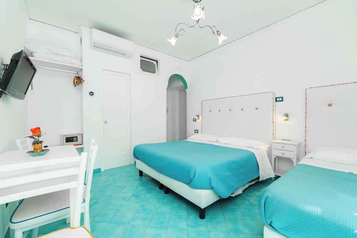 A room with two beds, a desk, a chair, a TV, and a small table with a vase.