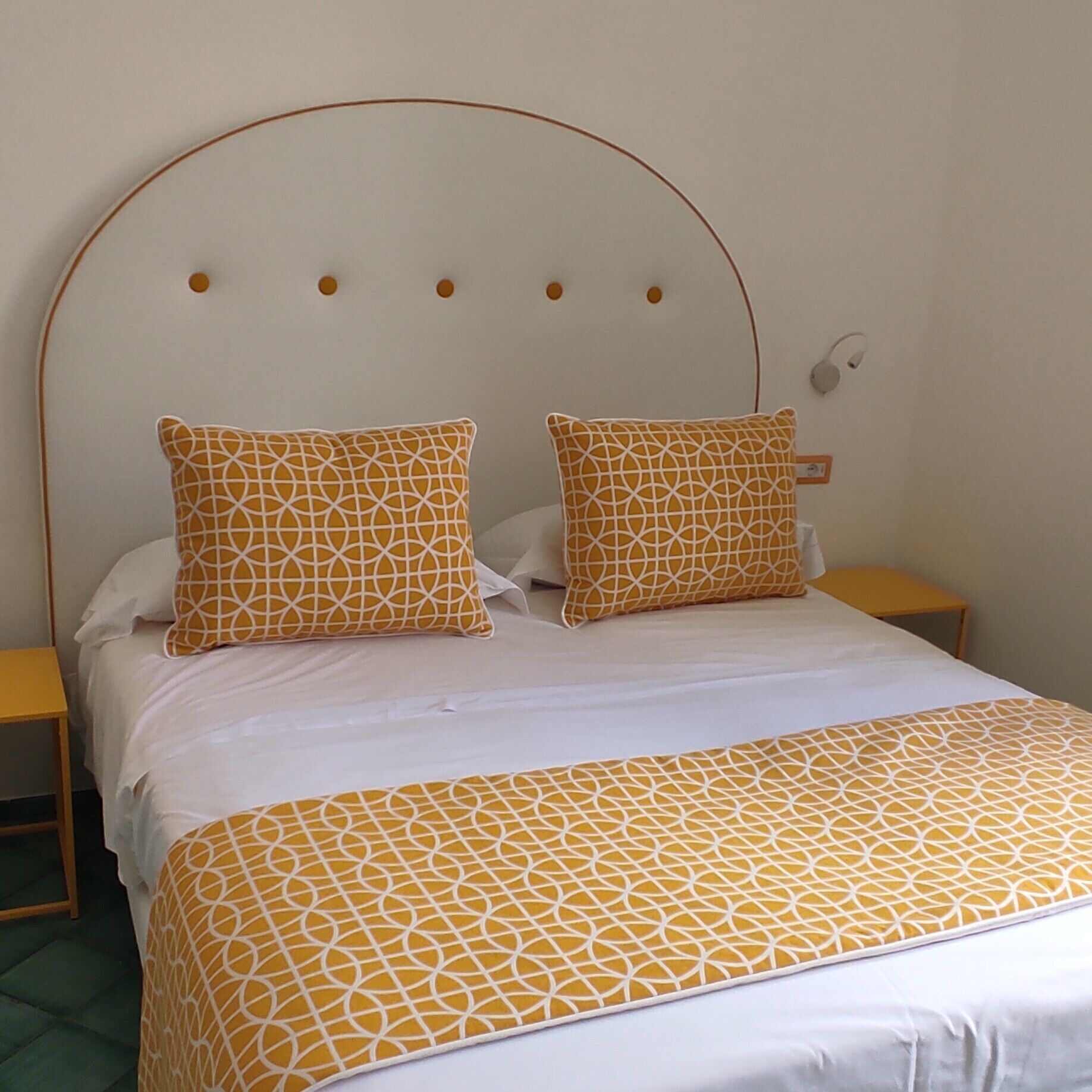 Un lit avec une couvre-lit et des oreillers à motifs géométriques, une tête de lit ornée de découpes circulaires et une table de chevet avec une lampe.
