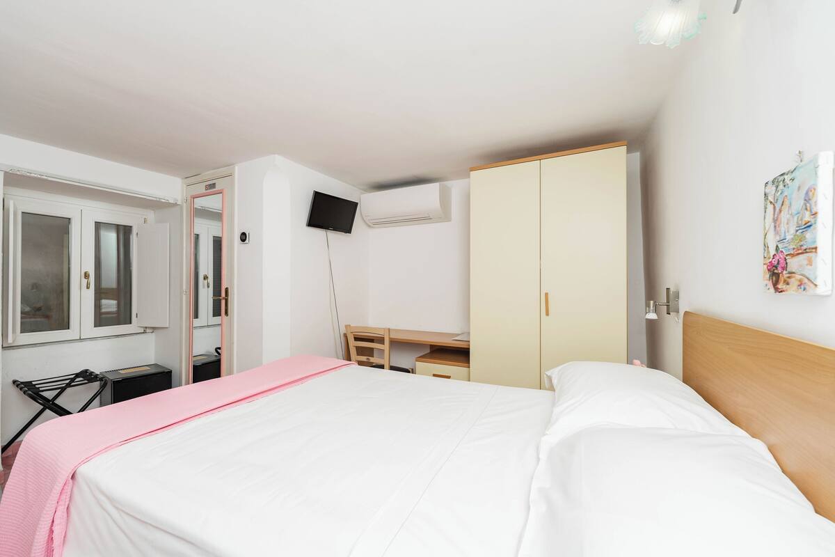 A bedroom with a bed, a desk, a wardrobe, and a television.