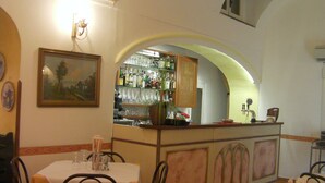 Interior de restaurante com área de bar, mesas com toalhas brancas e cadeiras.