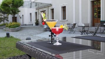 Pöydällä on kaksi juomaa, punainen ja keltainen cocktail, ja pöydän edessä on rakennus, jonka edessä on sisäpiha.
