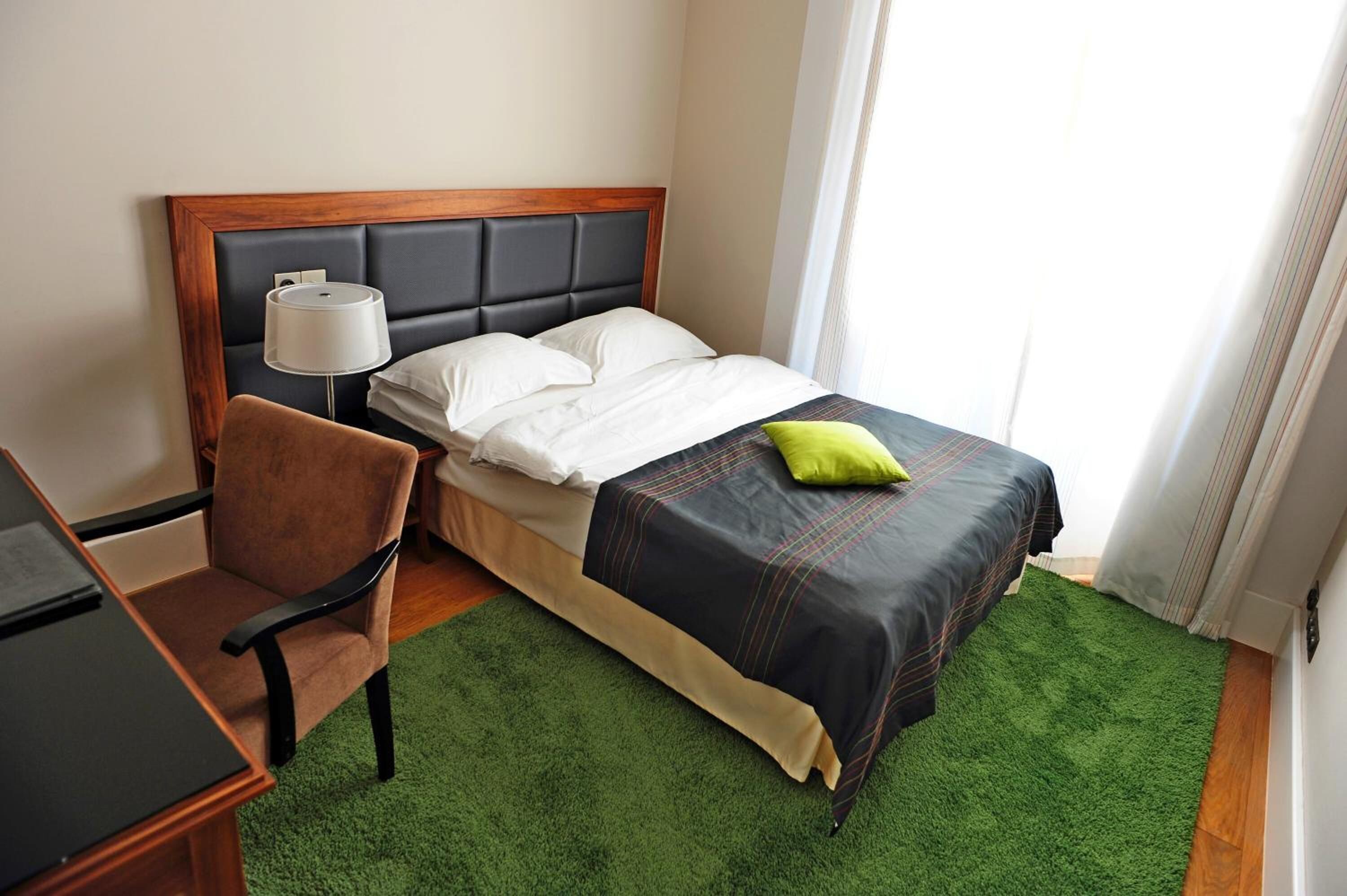 Une chambre d’hôtel avec un lit, un bureau, une chaise et une moquette verte.