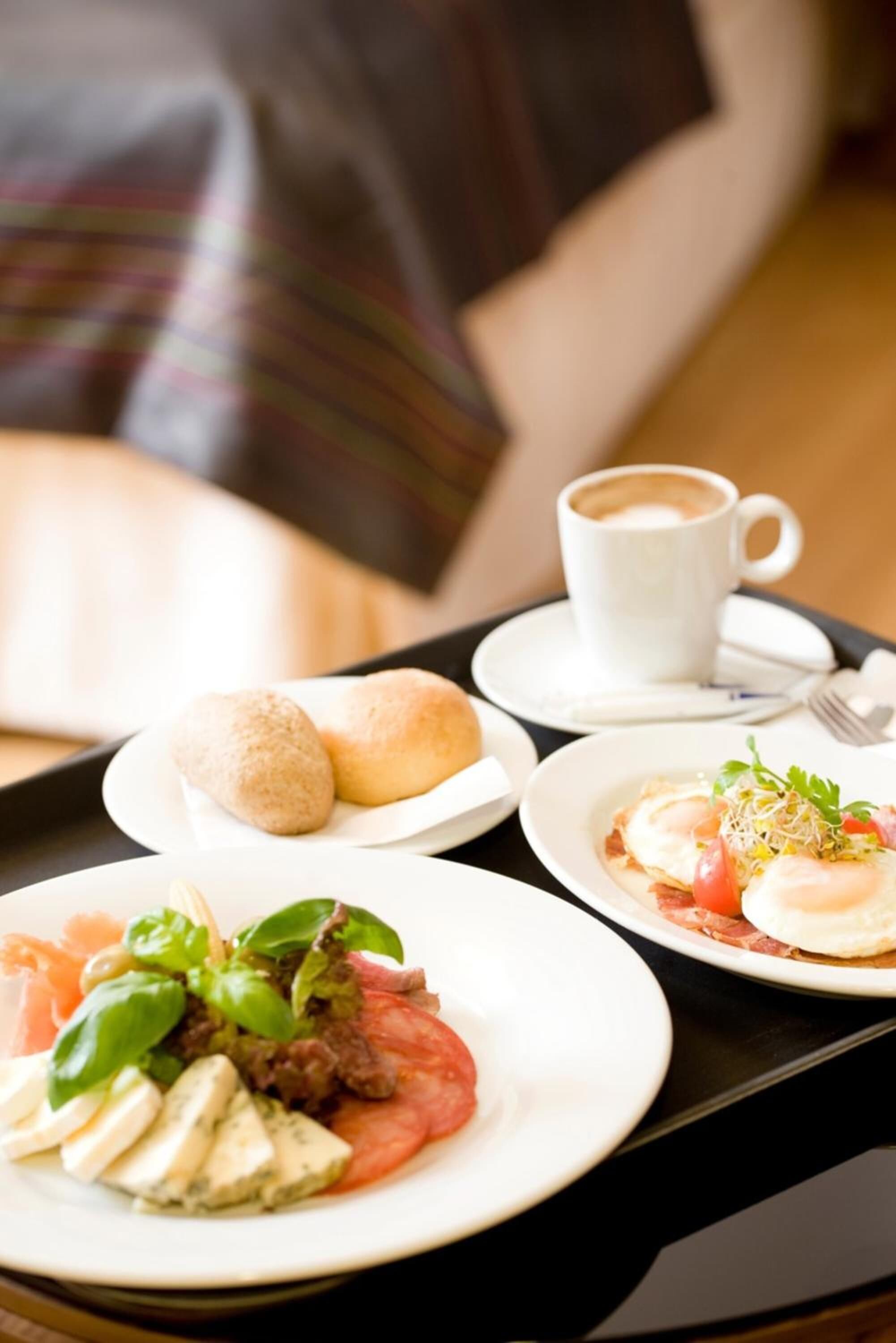 Bandeja con alimentos para el desayuno, incluyendo huevos, tomates, albahaca y una taza de café.