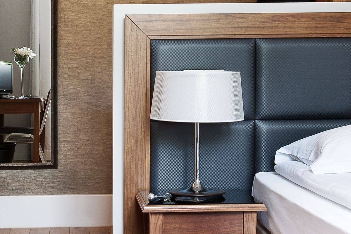 Una cama bien hecha con sábanas blancas, una lámpara de noche y una mesita de madera.