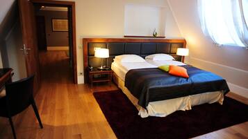 A bedroom with a bed, two bedside tables, a nightstand, a wooden headboard, a window with curtains, and a door leading to another room.