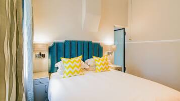A hotel room with a bed, two nightstands, a teal headboard, and two yellow and white patterned pillows.