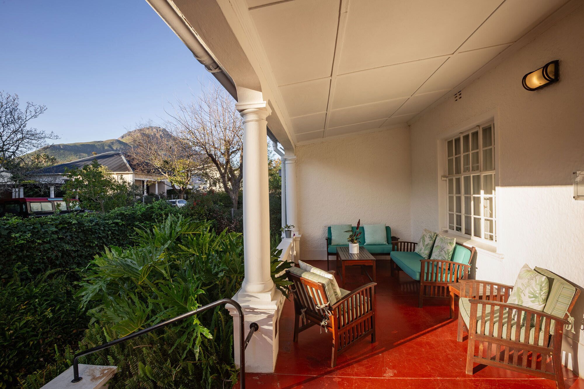 A covered porch with a red floor, white columns, and a seating area with wooden chairs and a green sofa.
