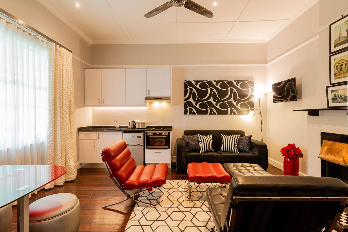 A modern living room with a sofa, ottoman, and a red chair. There is a kitchen area with cabinets and a microwave.