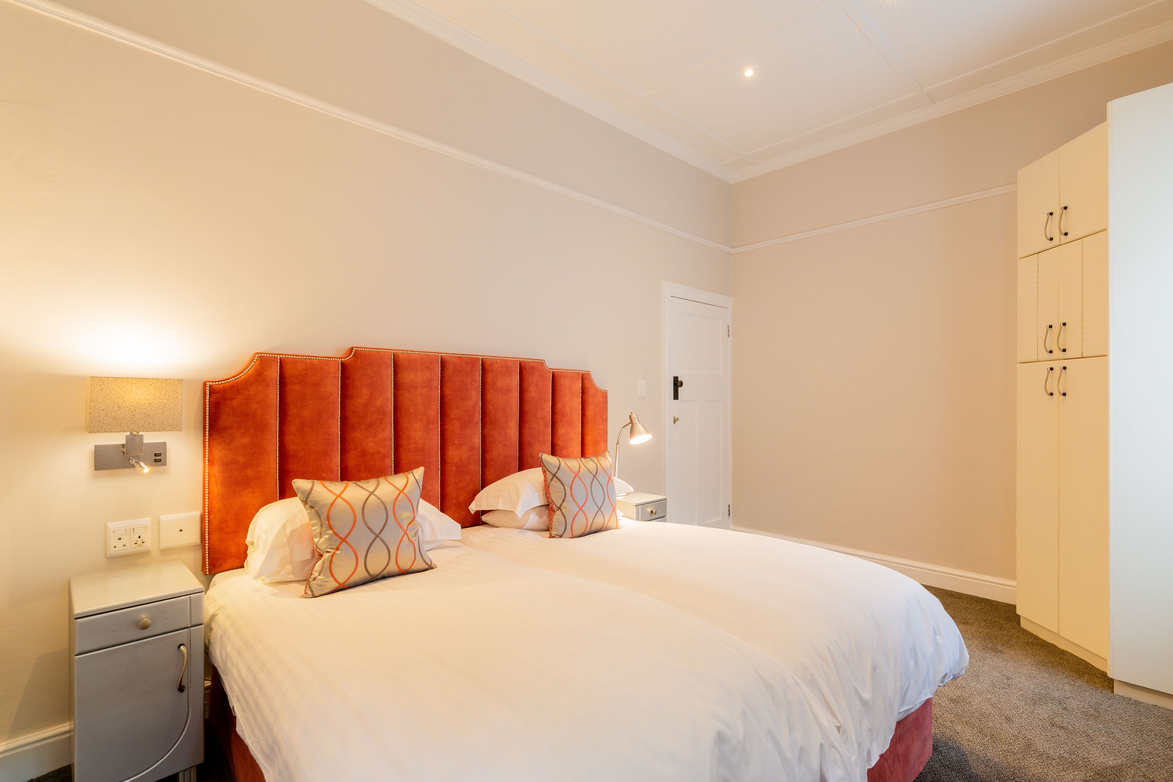 A neatly arranged bedroom with a large bed, a nightstand, a wardrobe, and a door.