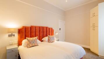 A neatly arranged bedroom with a large bed, a nightstand, a wardrobe, and a door.