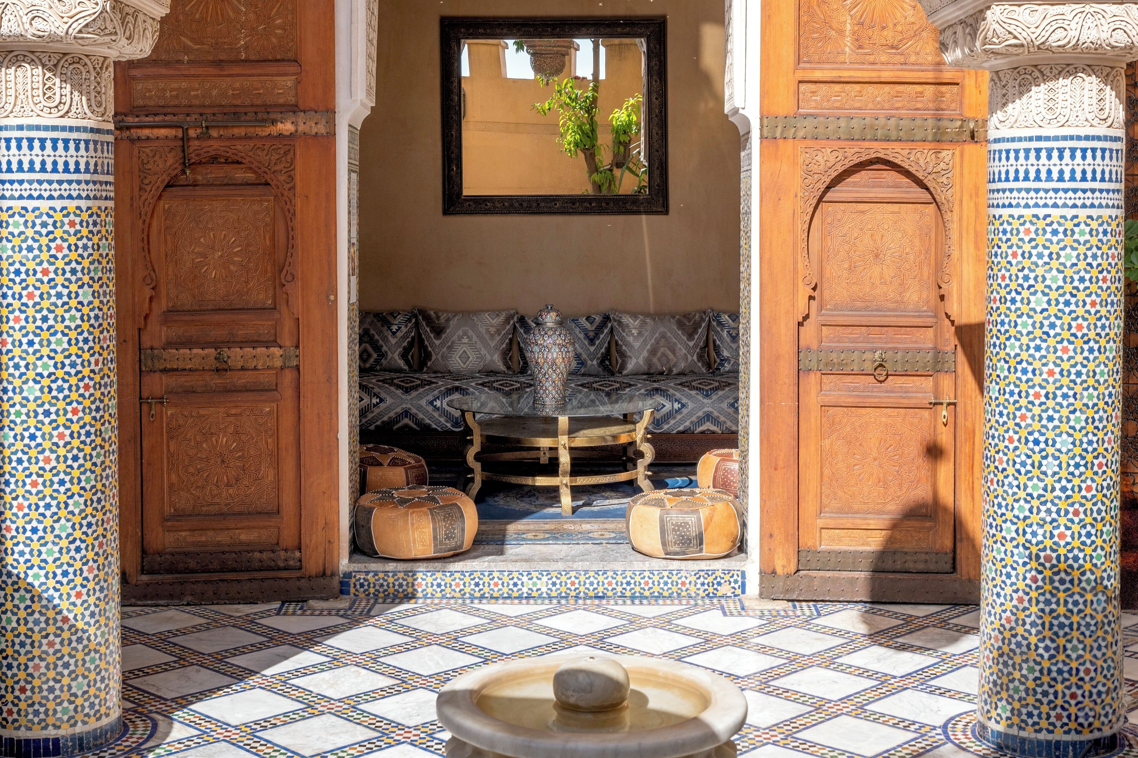 A traditional Moroccan interior with a tiled floor, a wooden bench, and a central fountain.