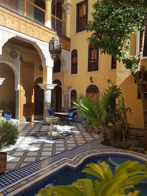 An indoor courtyard with a tiled pool, seating area, and ornate architectural details.