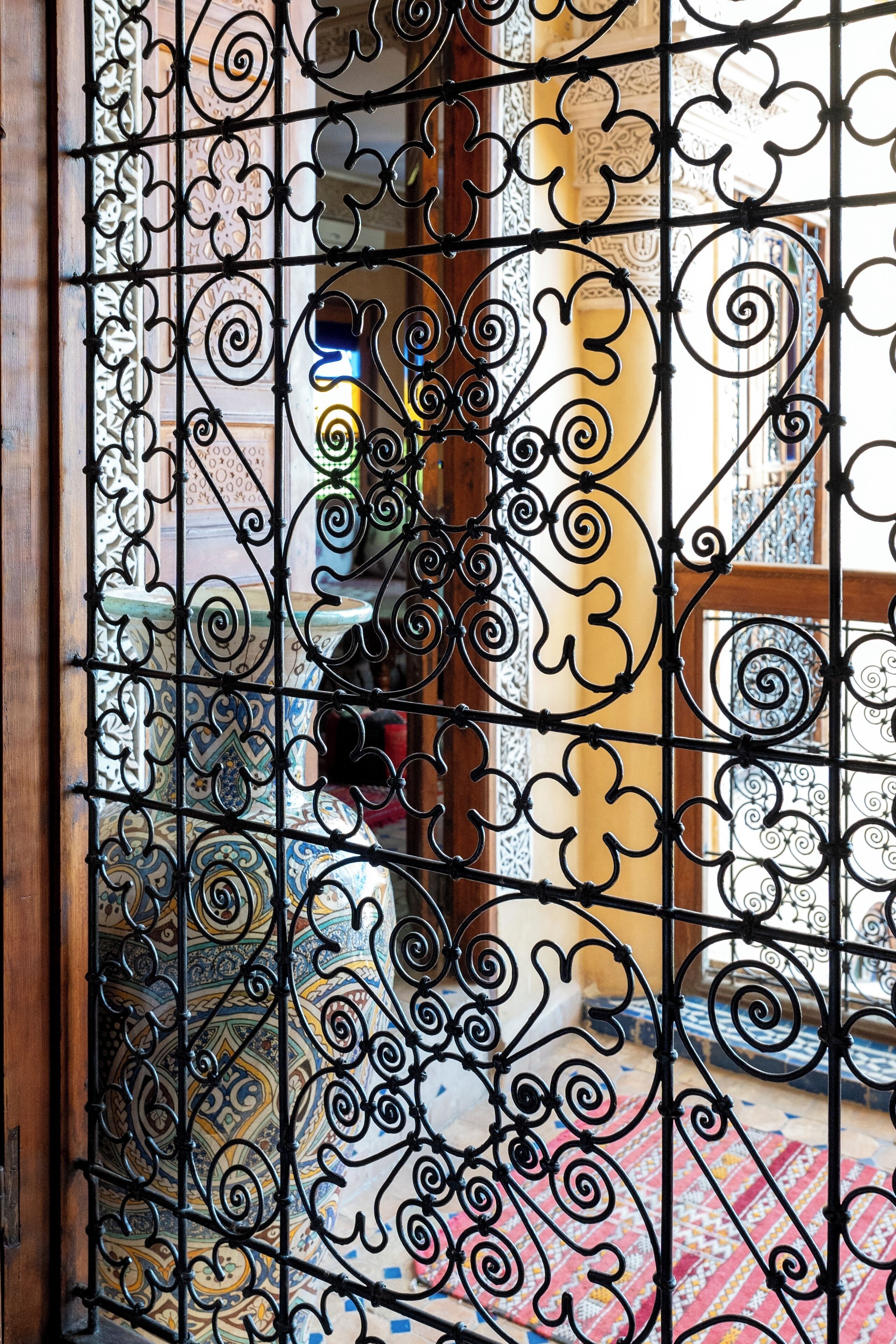 A wrought iron gate with intricate designs, leading to a room with patterned tiles and a wooden floor.