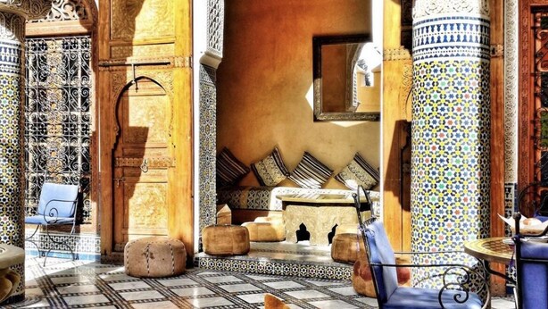 A traditional Moroccan interior with a tiled floor, a sofa set, and a table set with food and drinks.