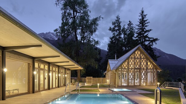 A modern outdoor pool area with a wooden deck, glass walls, and a wooden cabin-like structure.