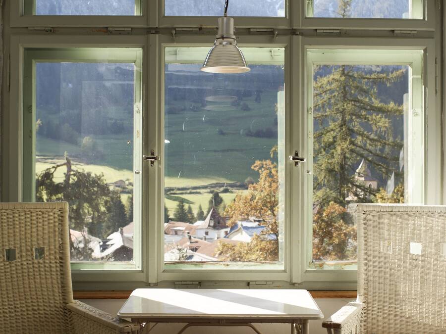 Une pièce dotée d’une grande fenêtre donnant sur un paysage montagneux, avec une table blanche et des chaises en osier.