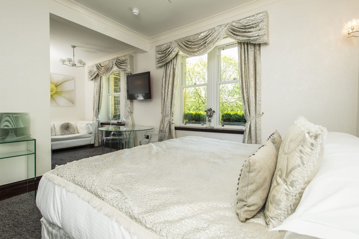 A bedroom with a large bed, a sofa, a TV, and a window with curtains.