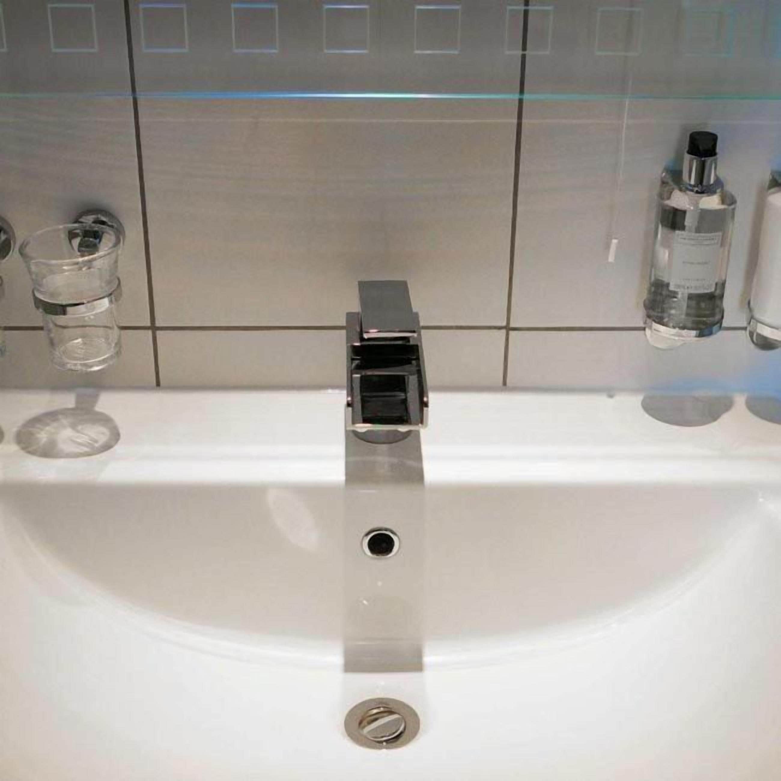 A bathroom sink with a modern faucet, a glass of water, and a bottle of hand soap on the counter.