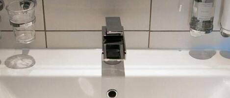 A bathroom sink with a modern faucet, a glass of water, and a bottle of hand soap on the counter.