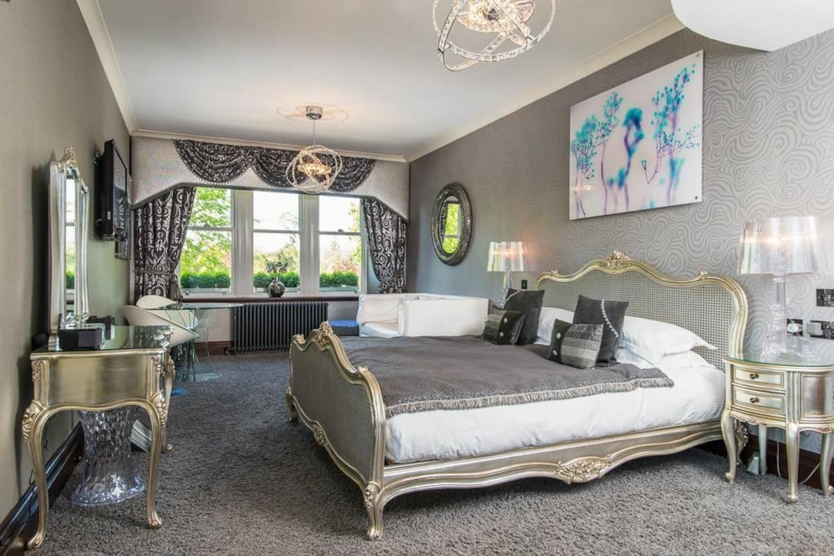 A bedroom with a large bed, a desk, and a window with curtains.