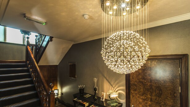 A staircase with a wooden handrail and carpeted steps, leading to a landing with a chandelier and a small table with books and a vase. - Windermere Suites (Windermere)