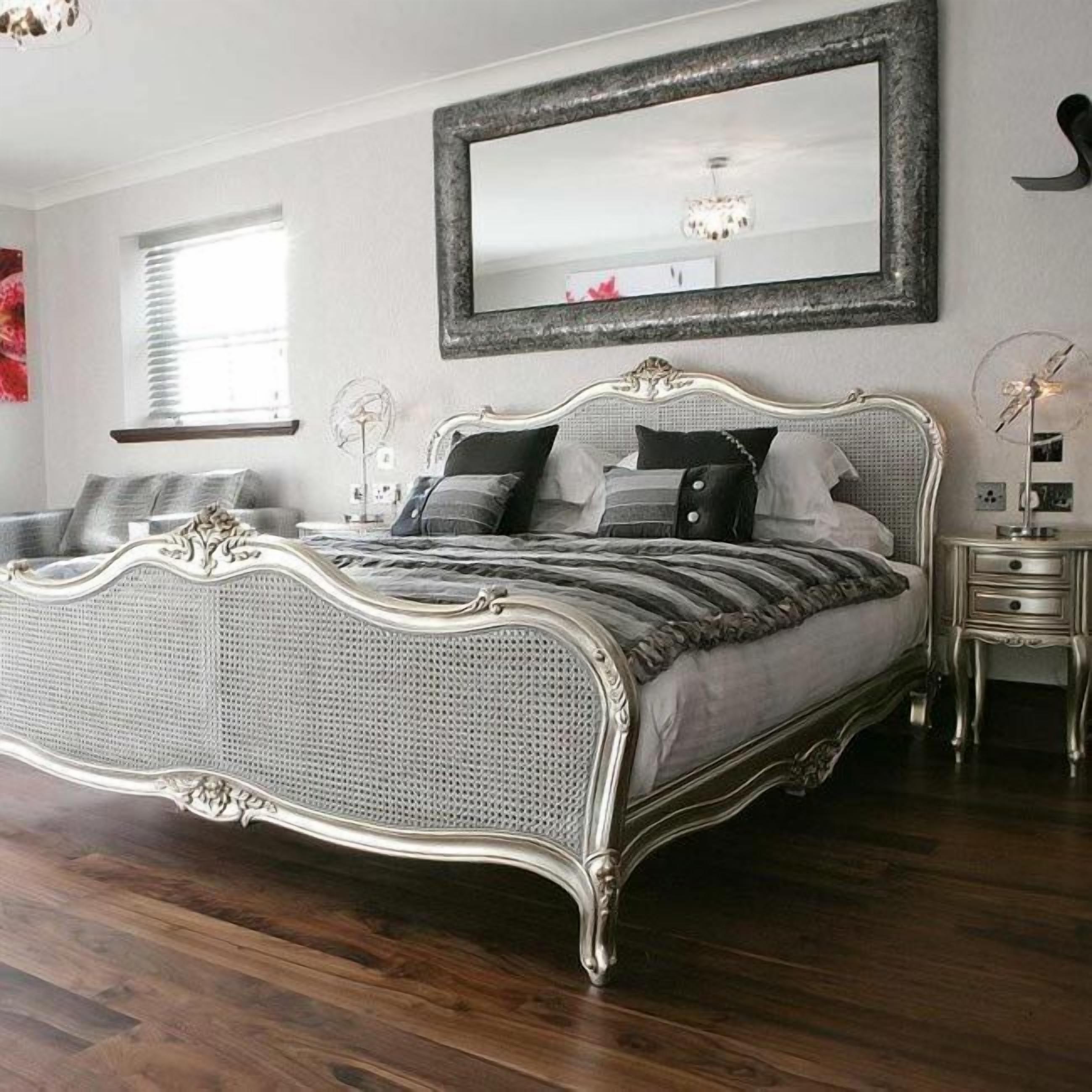 A bedroom with a classic four-poster bed, a large mirror, and a bedside table with a lamp.