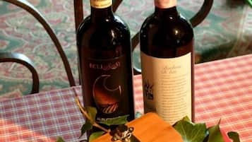 Due bottiglie di vino su un tavolo con tovaglia a quadri, circondato da foglie verdi e un tagliere di legno con un coltello.
