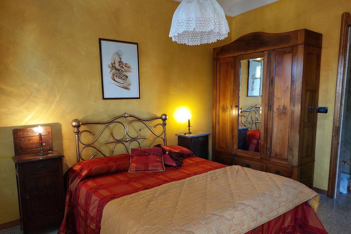 A bedroom with a bed, a wooden wardrobe, a nightstand, a lamp, and a framed picture on the wall.