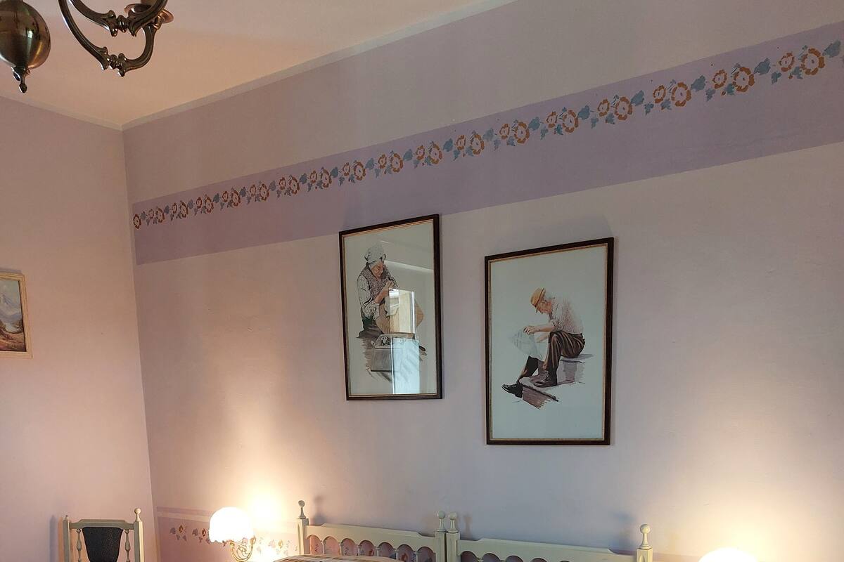 A bedroom with a large bed, two bedside tables with lamps, a chandelier, and floral wallpaper.