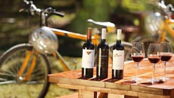 Una mesa de madera con botellas de vino y copas, colocada al aire libre con bicicletas al fondo.