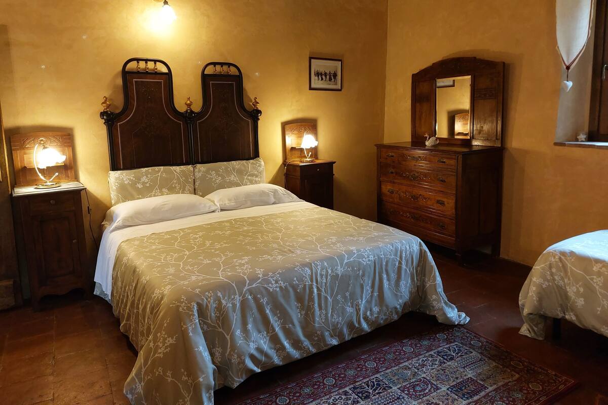 A bedroom with a large bed, two bedside tables with lamps, a dresser, a mirror, and a patterned rug.