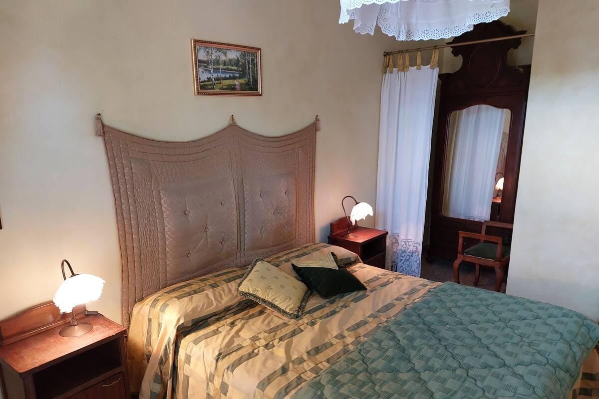 A bedroom with a wooden headboard, a bed with patterned bedding, a nightstand with a lamp, and a chair.