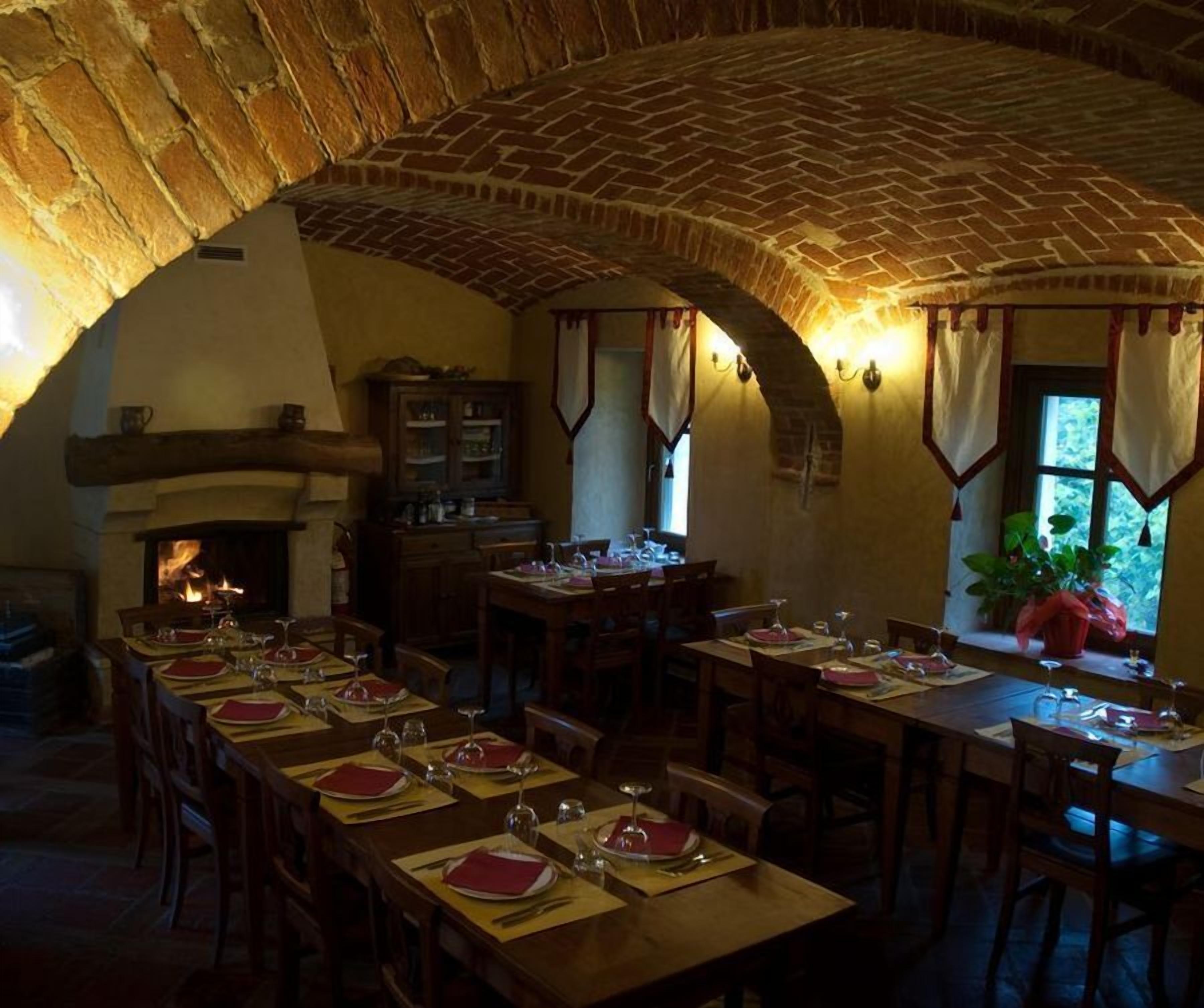 A dining area with brick arches, wooden tables set for dinner, and a fireplace.