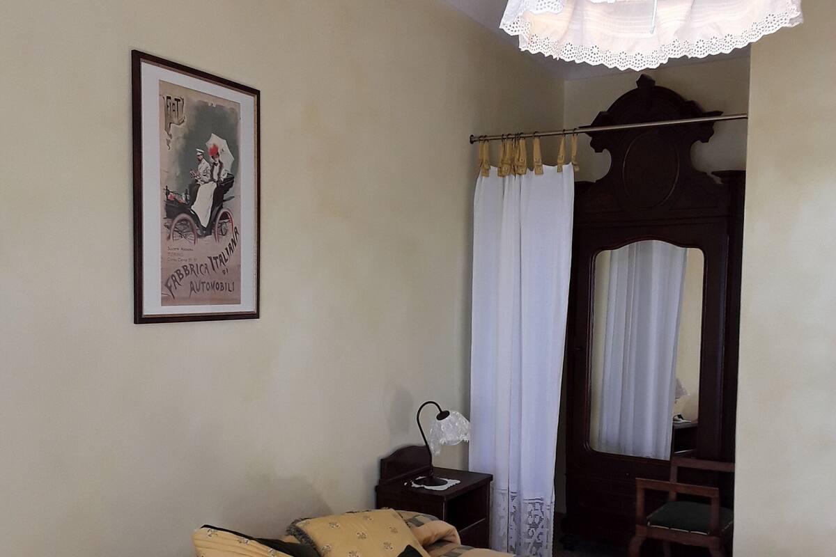 A bedroom with a bed, a bedside table, a lamp, a mirror, and a framed picture on the wall.