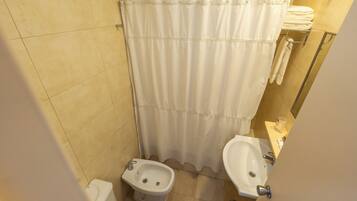 A small bathroom with a shower curtain, a bidet, a sink, and a towel rack.