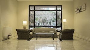 A modern living room with a sofa set, two armchairs, a coffee table, and a large window offering a view of trees and buildings. - Austral Express (Comodoro Rivadavia)