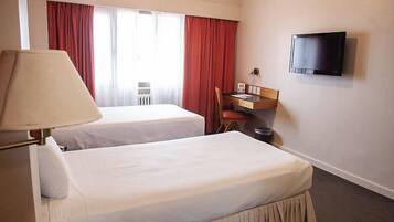 Een hotelkamer met twee bedden, een bureau, een stoel, een televisie en een plafondventilator.
