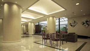 A spacious lobby with a high ceiling, large columns, and a seating area with chairs and a sofa. - Austral Express (Comodoro Rivadavia)