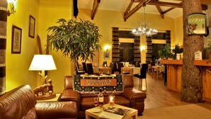 A cozy hotel lobby with leather furniture, a large plant, and a sign reading "Adirondack Mountains." - Albirondack Park Camping Lodge and Spa (Albi)