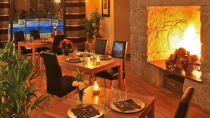 A dining area with a stone wall, a mounted moose head, a fireplace, and a view of a pool through large windows. - Albirondack Park Camping Lodge and Spa (Albi)