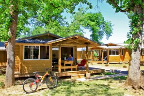 A wooden cabin with a porch, a bicycle, and a person sitting at the table.
