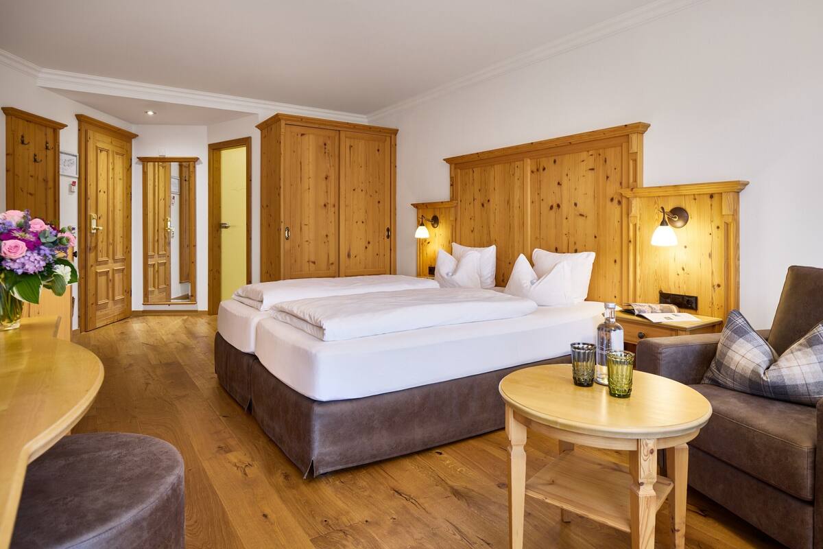 Un dormitorio con una cama grande, armario de madera, lámparas de noche, una mesita y un sofá.