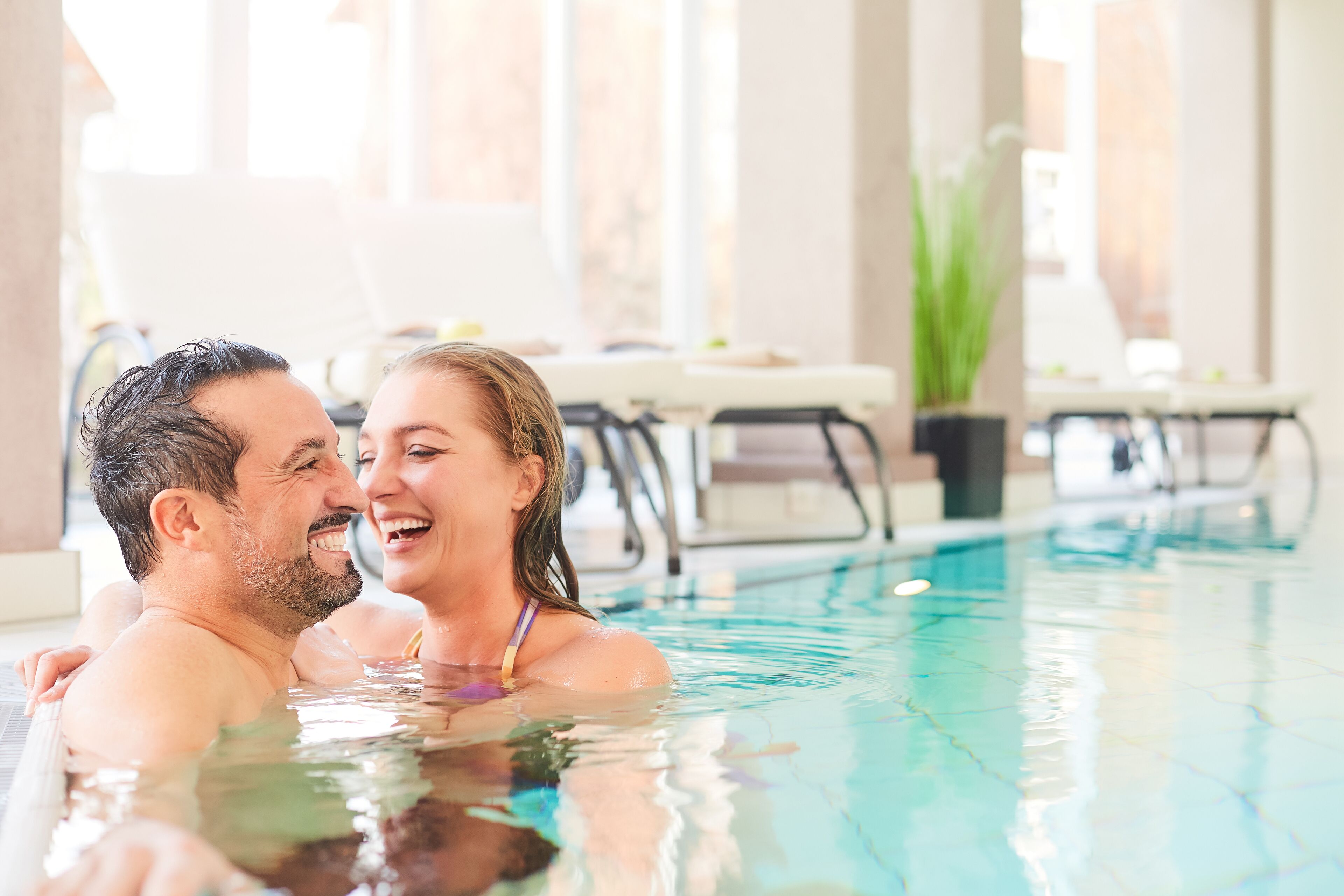 Ein Paar im Pool mit Liegestühlen und einer Pflanze im Hintergrund.