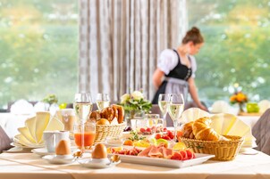 Un bufé de desayuno con diversas comidas y bebidas, incluyendo bollería, frutas y una selección de quesos.