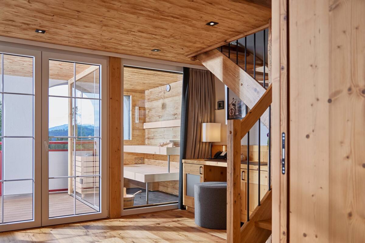 Interior de madera con una escalera, un escritorio y vistas a través de puertas de cristal.