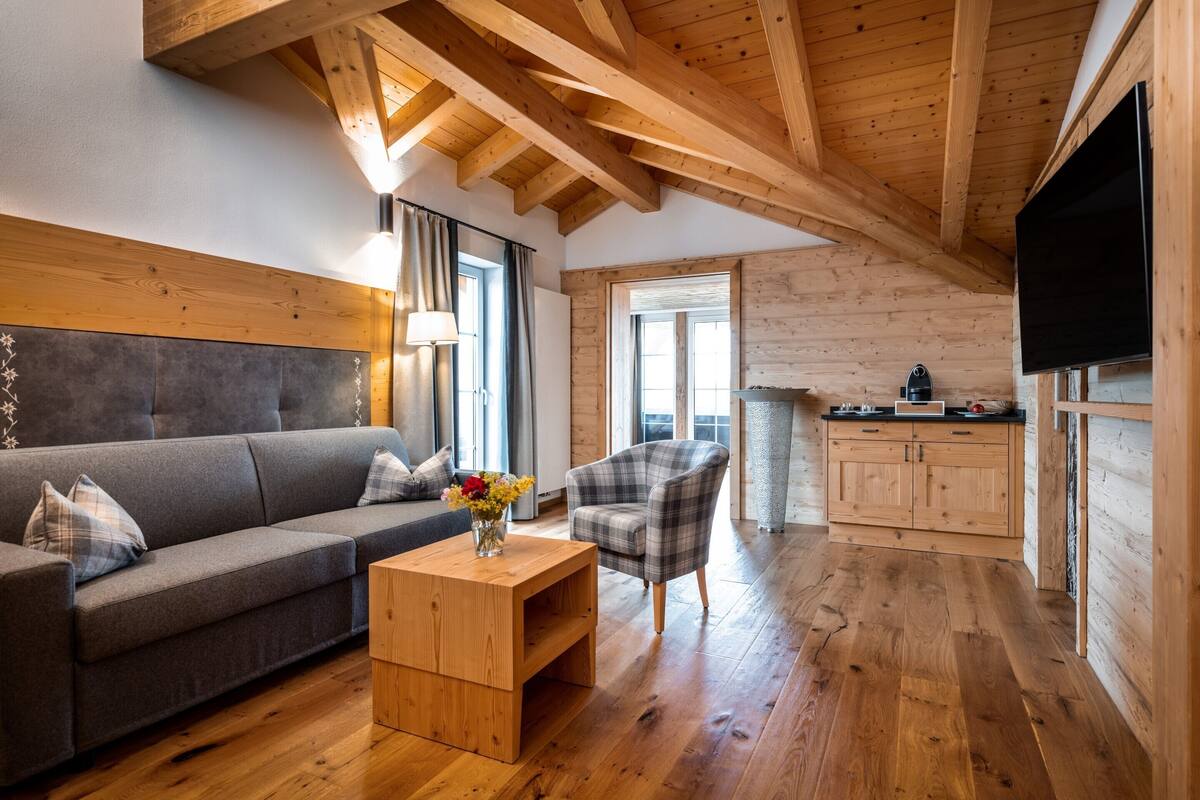 Una sala de estar moderna con un sofá, un sillón de cuadros, una mesa de centro de madera y un televisor montado en la pared.