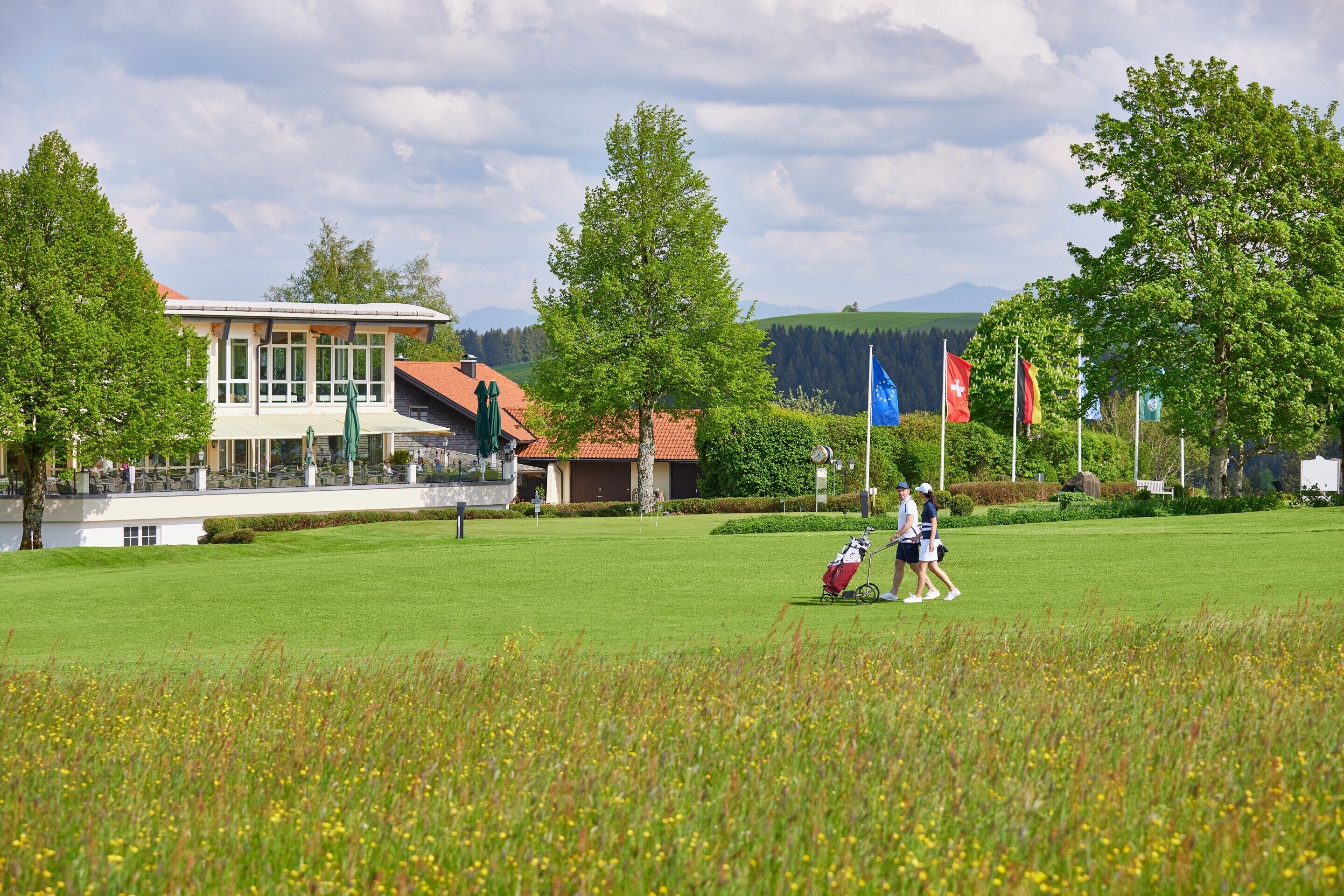 Ein Golfplatz mit einem Gebäude im Hintergrund, Flaggen und blauem Himmel.