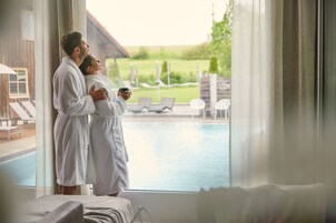 Una pareja con batas blancas de pie junto a una ventana con vista a una piscina.