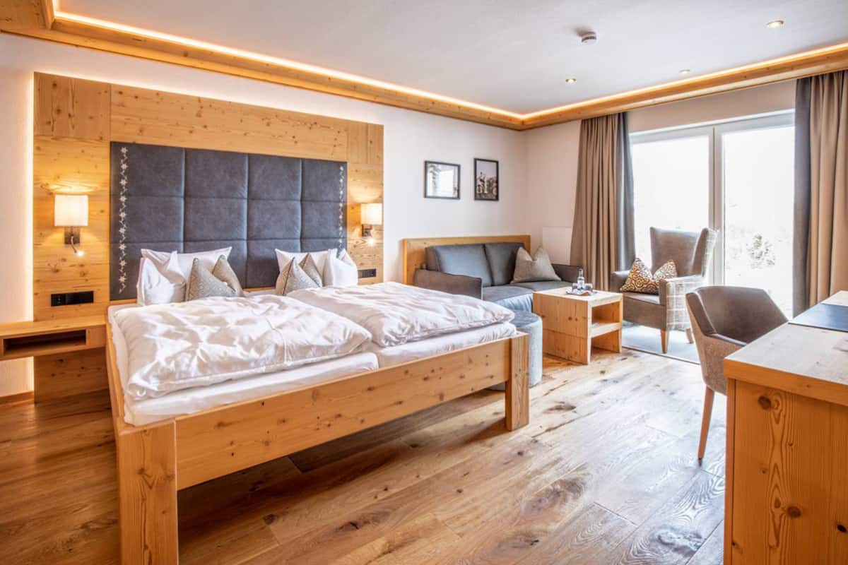 Habitación de hotel con una cama de madera, un escritorio, una silla y un ventanal grande.