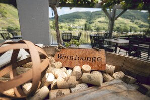 A Weinlounge with a view of green hills and a wooden table with a sign. - Weinhaus Halfenstube (Senheim)